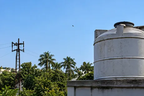 A water tank up on a rooftop, against palm trees and a clear sky